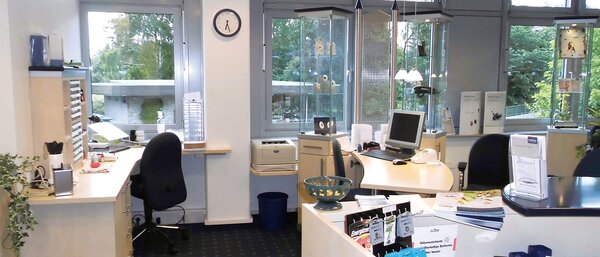 Modernes, helles Büro mit Schreibtischen, Computer, Broschüren und großen Fenstern.